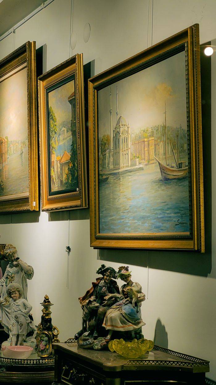 An art gallery showcasing framed paintings and elegant porcelain figurines illuminated under soft lighting.