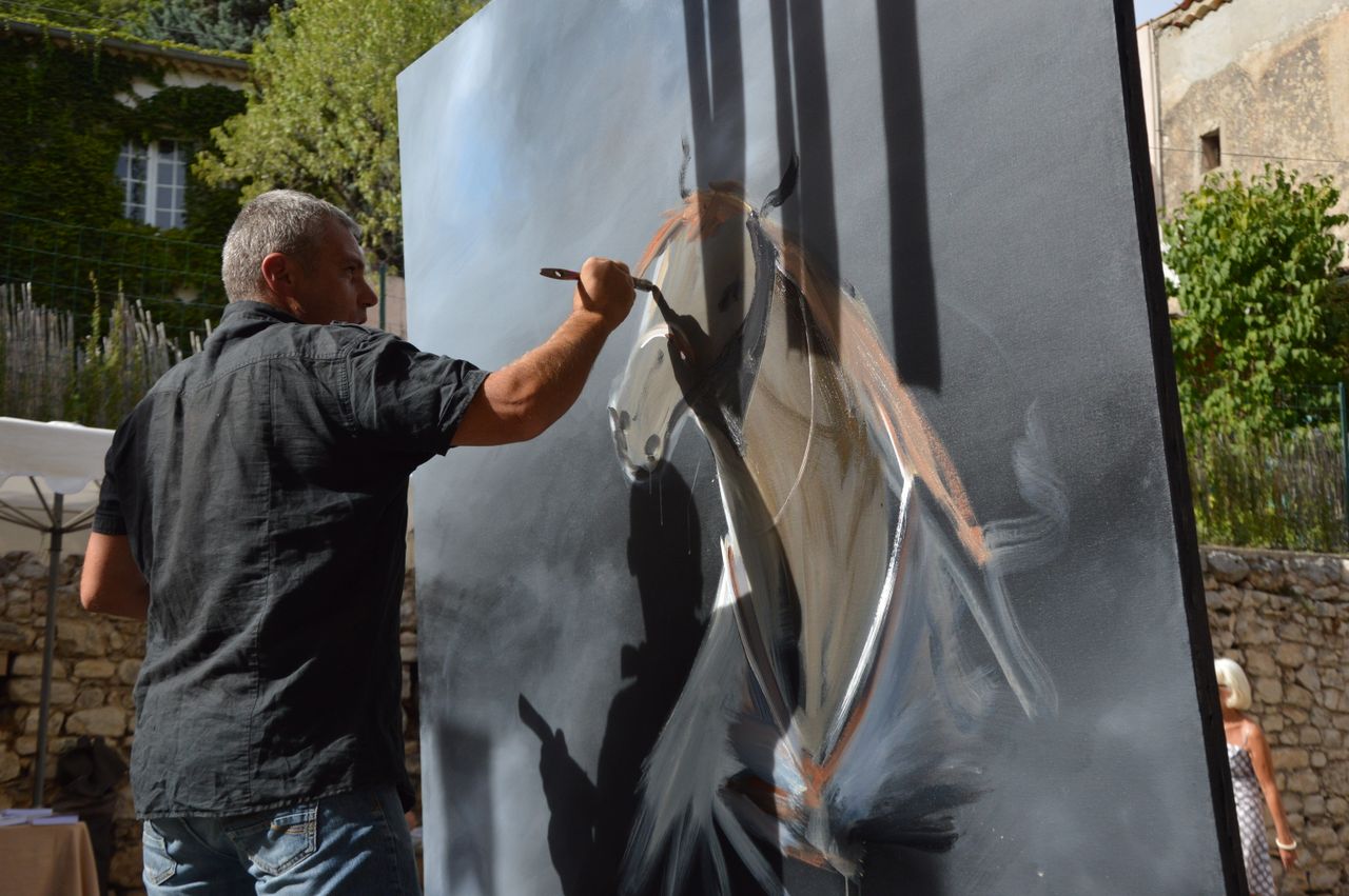 A man painting a horse on a canvas in an outdoor setting with natural light.