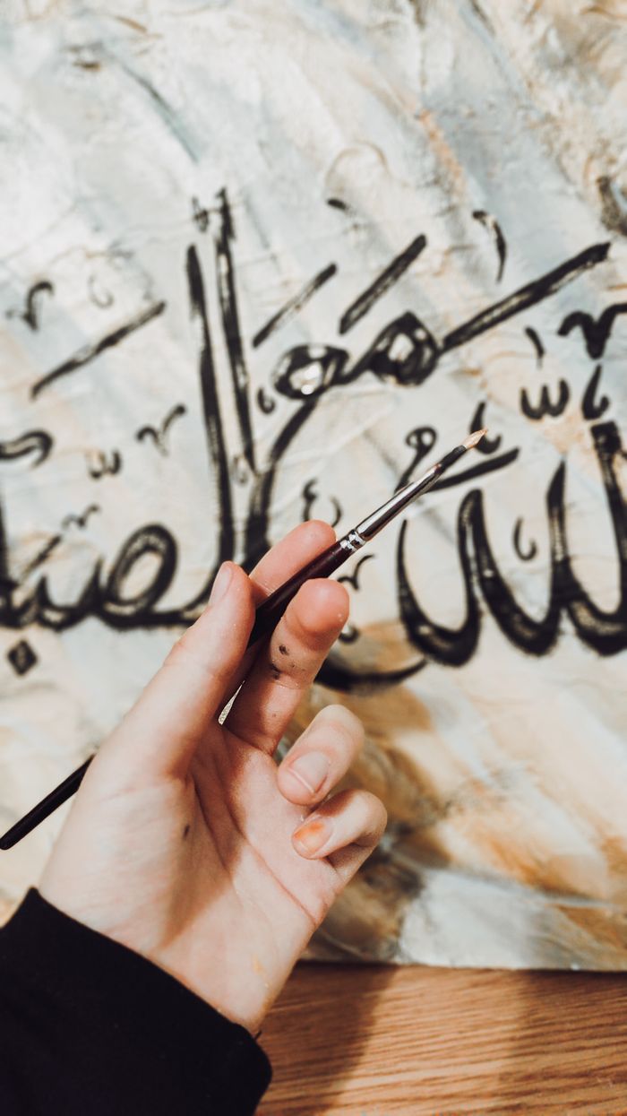 Close-up of a hand painting elegant Arabic calligraphy with a brush on canvas.