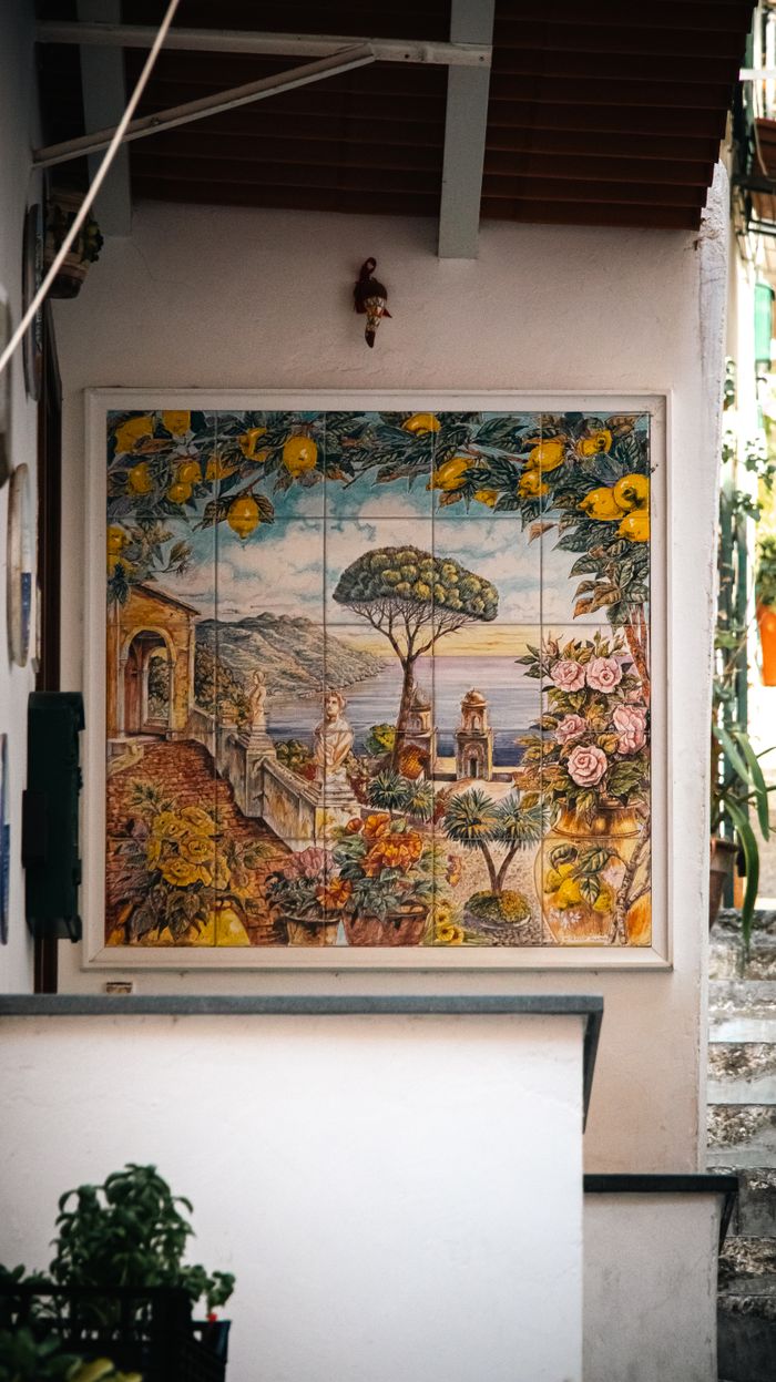 Vibrant ceramic mural depicting Amalfi Coast scenery on a sunny street wall.