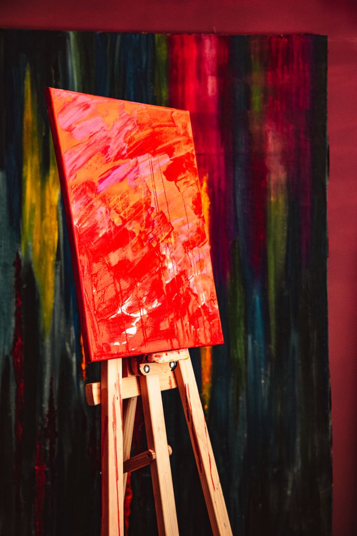A colorful abstract painting displayed on a wooden easel with a textured, expressive backdrop.